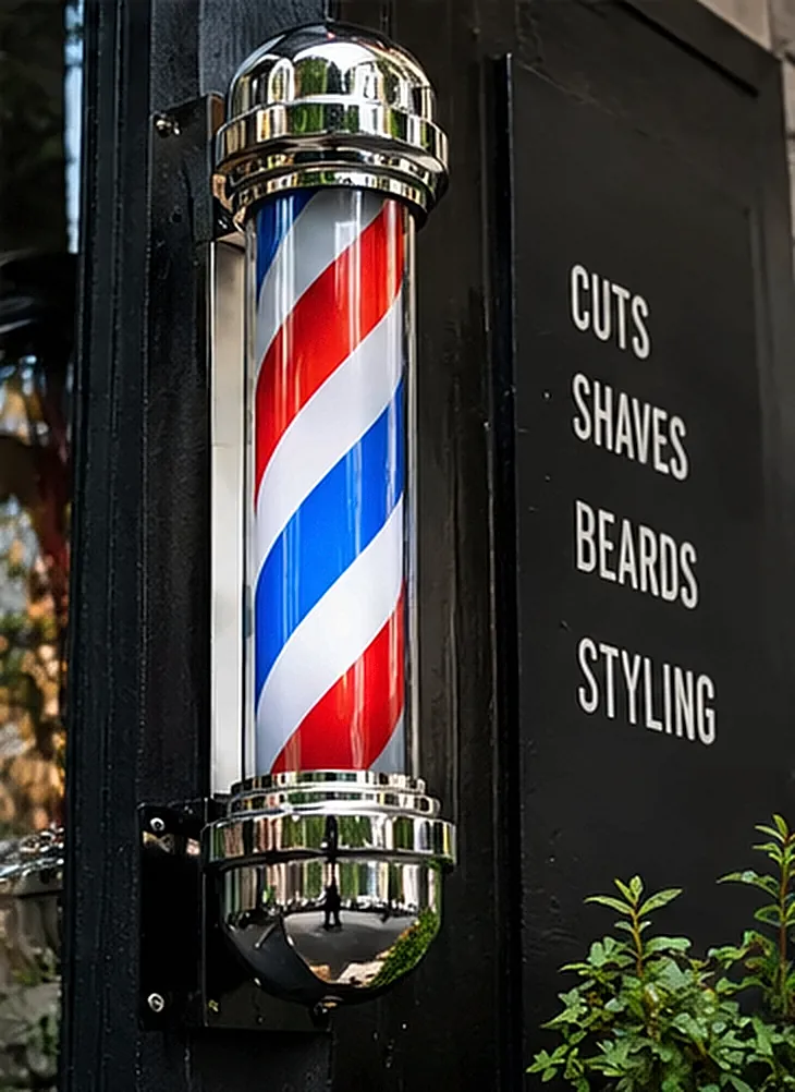 Friseurpfahl in Rot, Weiß und Blau neben der Tafel Cuts, Shaves, Beards, Styling